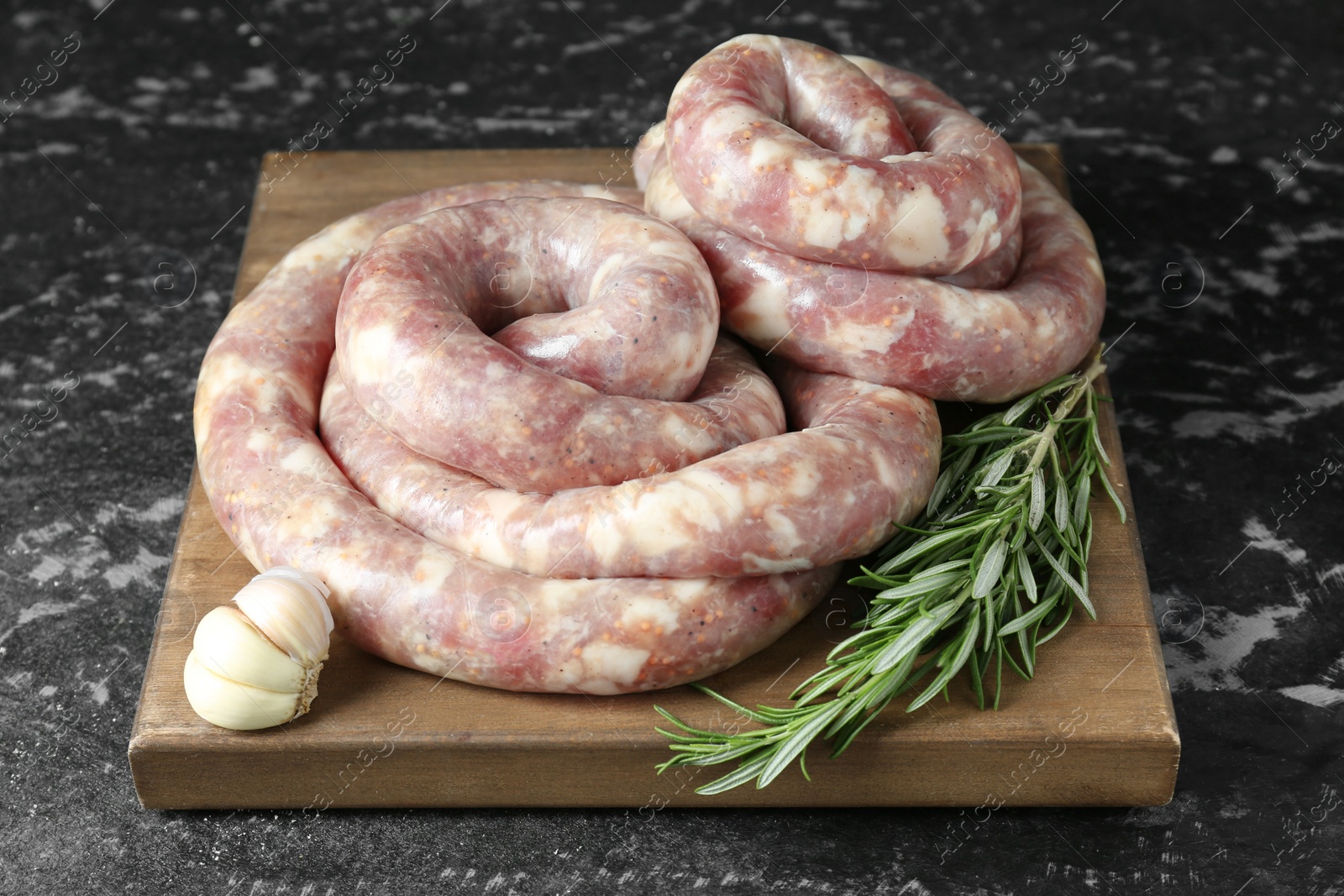 Photo of Raw homemade sausage, rosemary and garlic on grey textured table, closeup