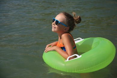 Photo of Happy little girl with sunglasses and inflatable ring in sea on sunny day. Beach holiday