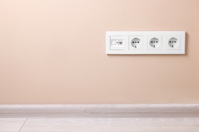 Electric power sockets on beige wall, space for text