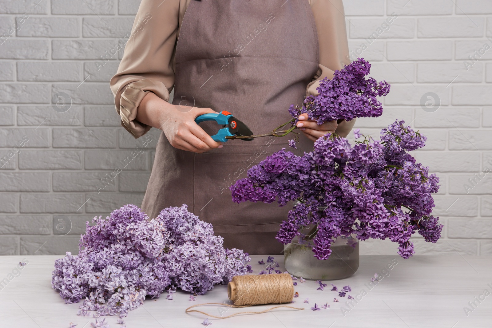 Photo of Woman trimming lilac branches with secateurs at white wooden table, closeup