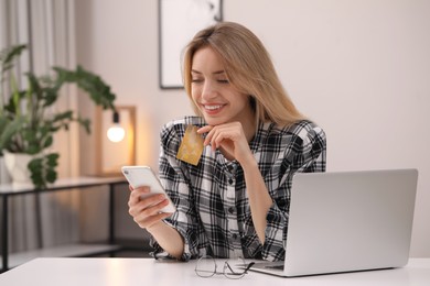 Photo of Woman with credit card using smartphone for online shopping at white table indoors