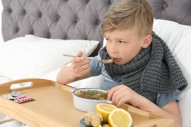 Photo of Sick little boy eating broth to cure cold in bed at home