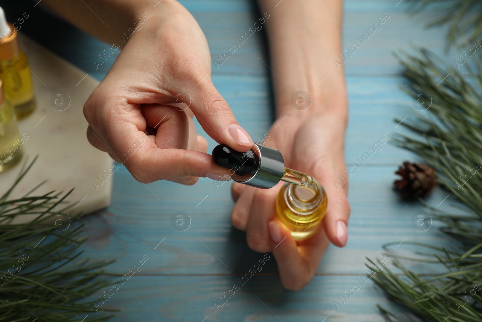 Photo of Woman holding bottle with pine essential oil at light blue wooden table, closeup