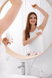 Beautiful young woman applying deodorant in bathroom