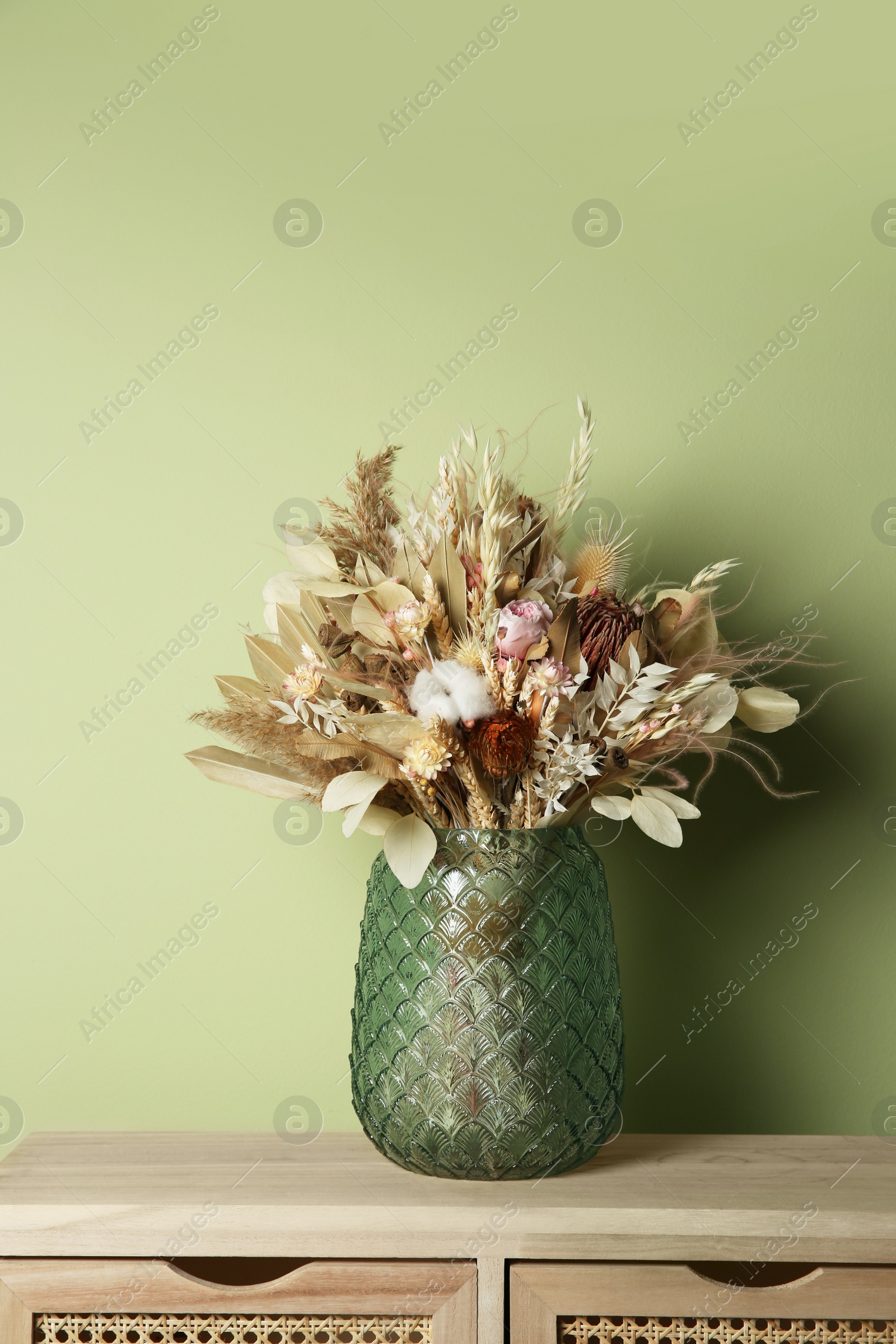 Photo of Beautiful dried flower bouquet in glass vase on wooden table near olive wall