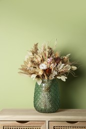 Beautiful dried flower bouquet in glass vase on wooden table near olive wall