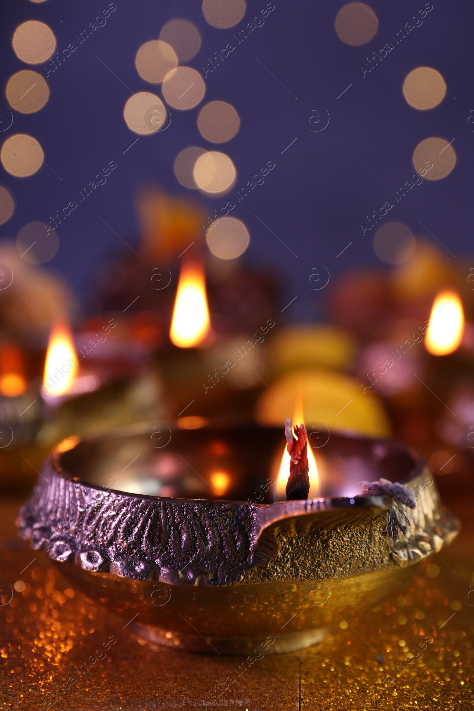 Photo of Diwali celebration. Diya lamp on shiny golden table against blurred lights, closeup