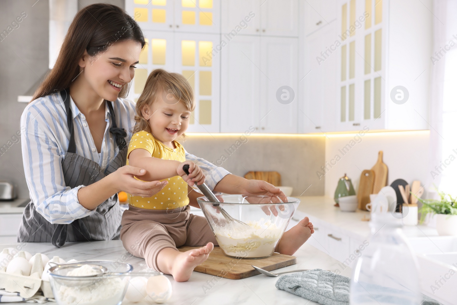 Photo of Mother and her little daughter cooking dough together in kitchen