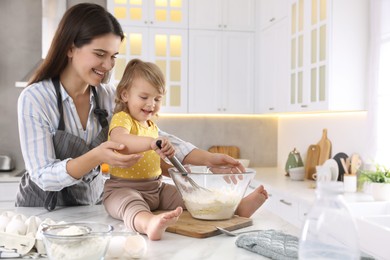 Photo of Mother and her little daughter cooking dough together in kitchen