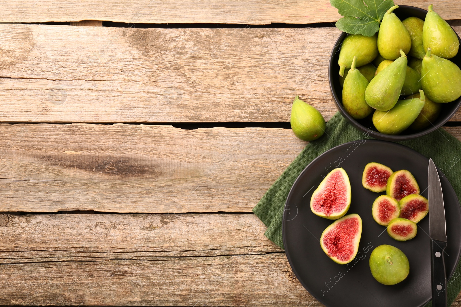 Photo of Cut and whole green figs with knife on wooden table, flat lay. Space for text