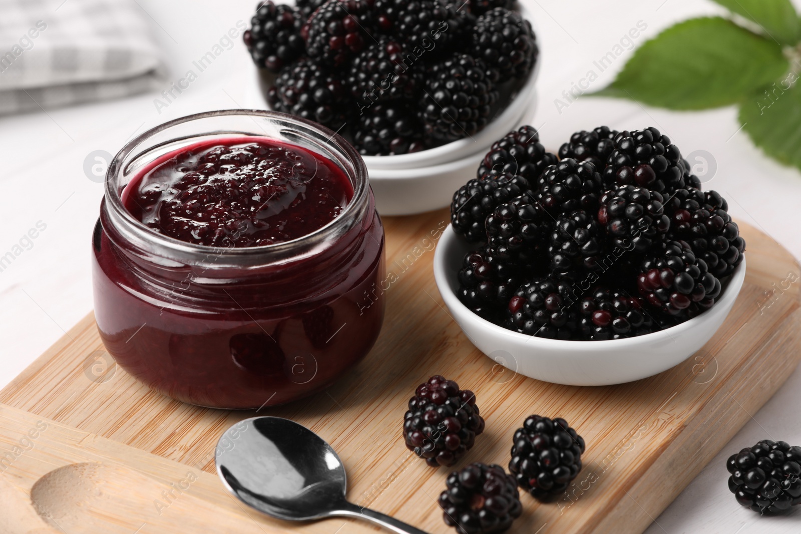 Photo of Fresh ripe blackberries and tasty jam on wooden board, closeup