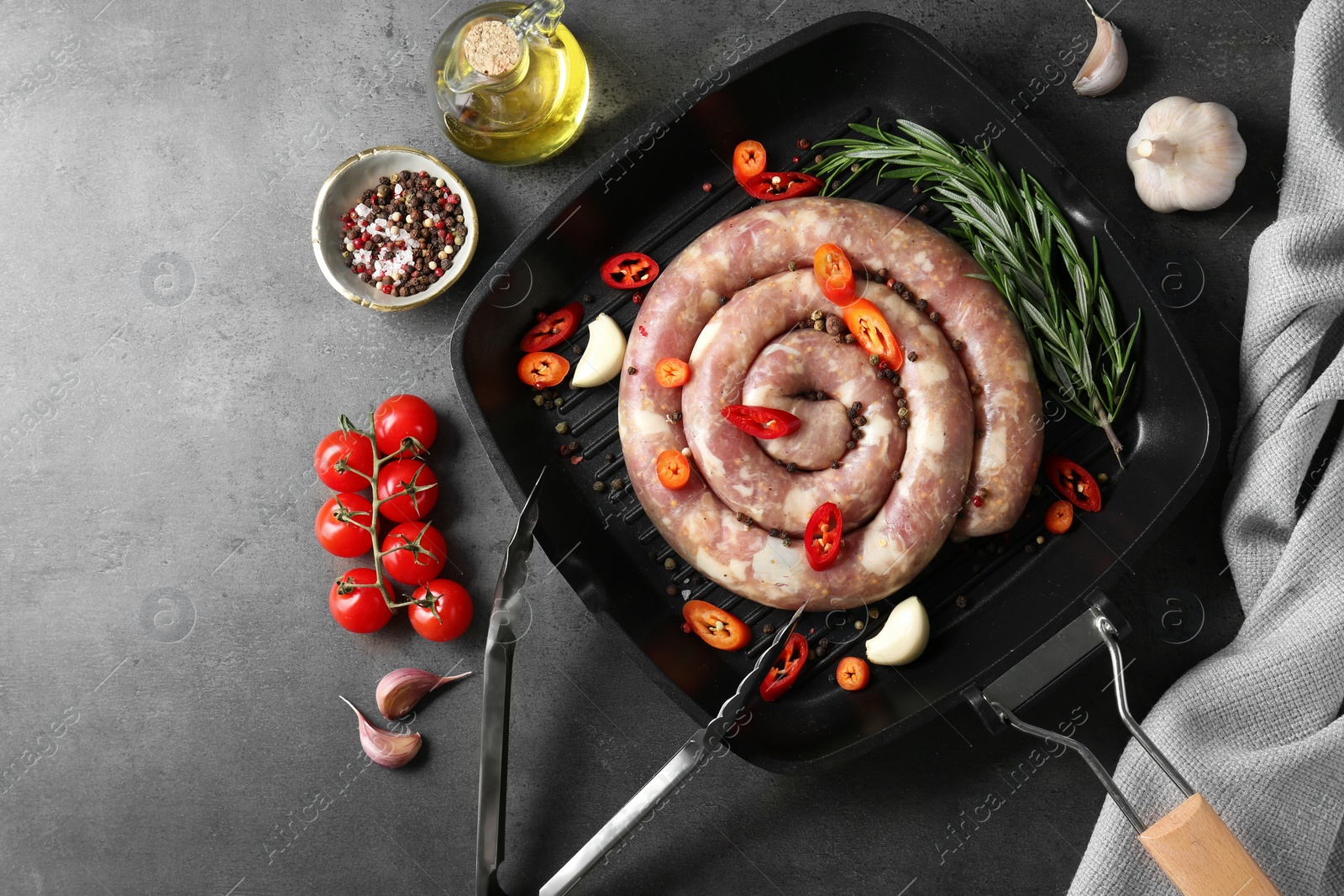 Photo of Pan with raw homemade sausage, spices, oil and tomatoes on grey table, flat lay