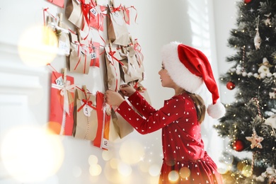 Image of Cute little girl in Santa hat taking gift from Christmas advent calendar at home. Bokeh effect