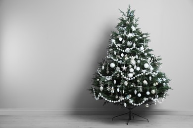Beautifully decorated Christmas tree near light grey wall in room, space for text