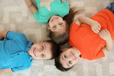 Photo of Cute little children lying together on floor in playing room, top view