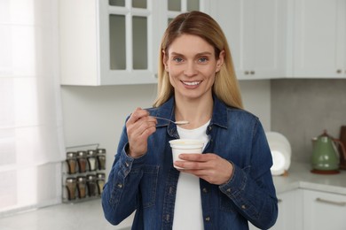 Photo of Woman eating tasty yogurt with spoon in kitchen