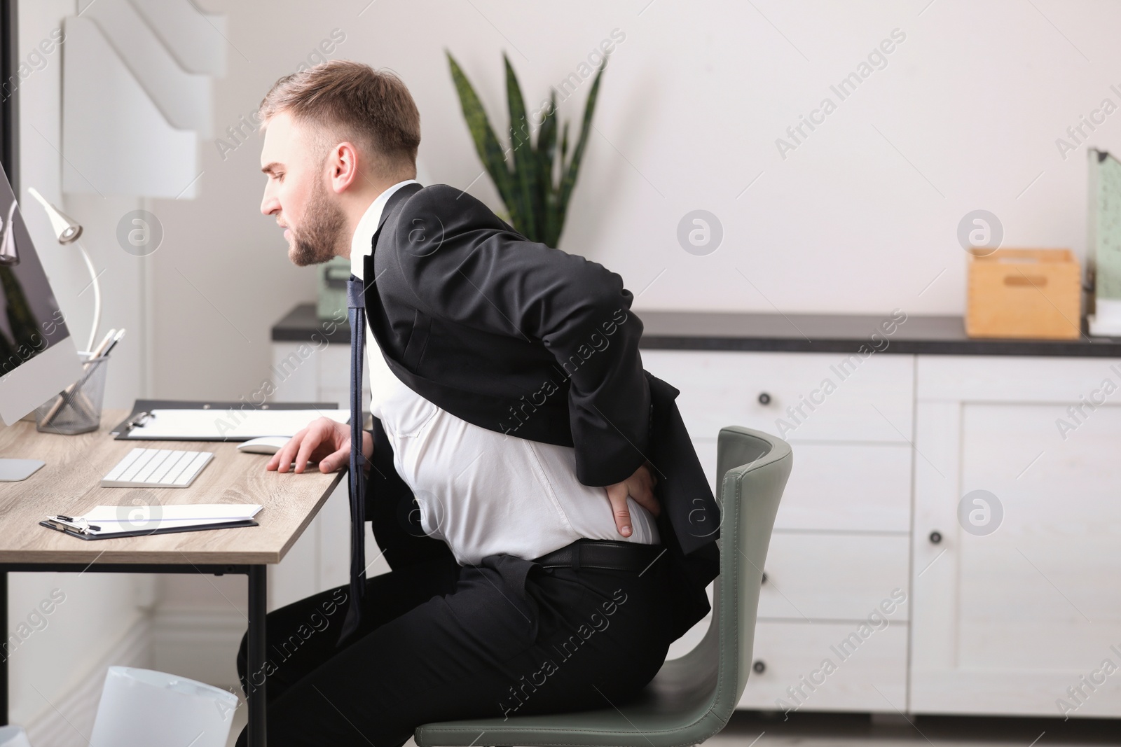 Photo of Businessman suffering from back pain at workplace