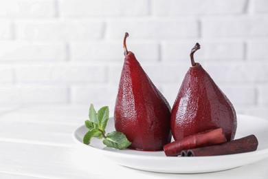 Tasty red wine poached pears with mint and cinnamon on white wooden table, closeup