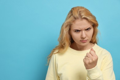 Aggressive young woman showing fist on light blue background. Space for text