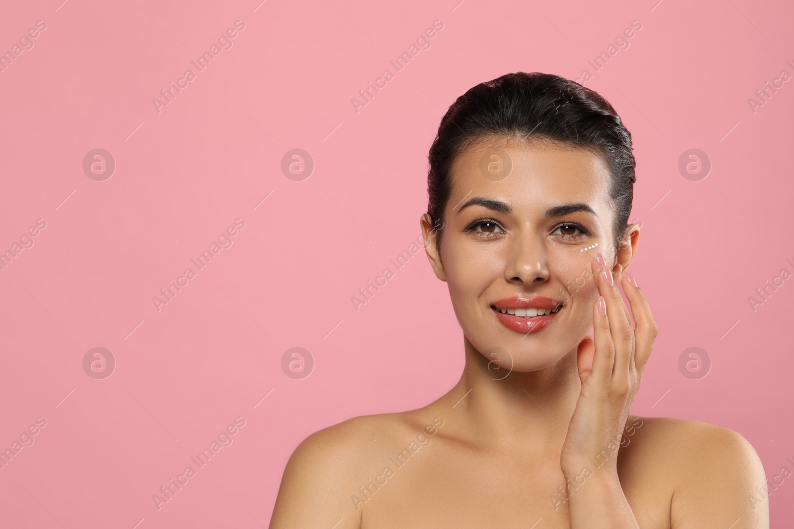 Photo of Woman applying cream under eyes on pink background, space for text. Skin care