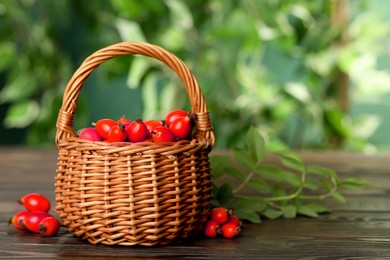 Ripe rose hip berries with green leaves on wooden table outdoors. Space for text