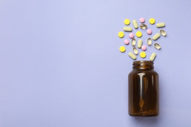 Bottle and different vitamin pills on violet background, top view. Space for text