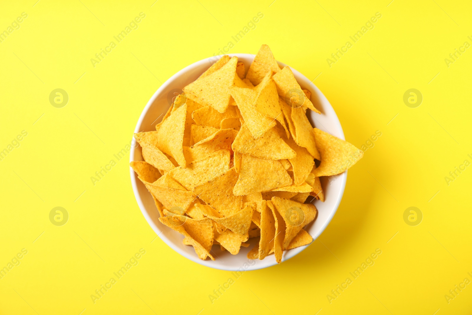 Photo of Tasty mexican nachos chips in bowl on yellow background, top view