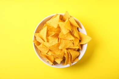 Tasty mexican nachos chips in bowl on yellow background, top view