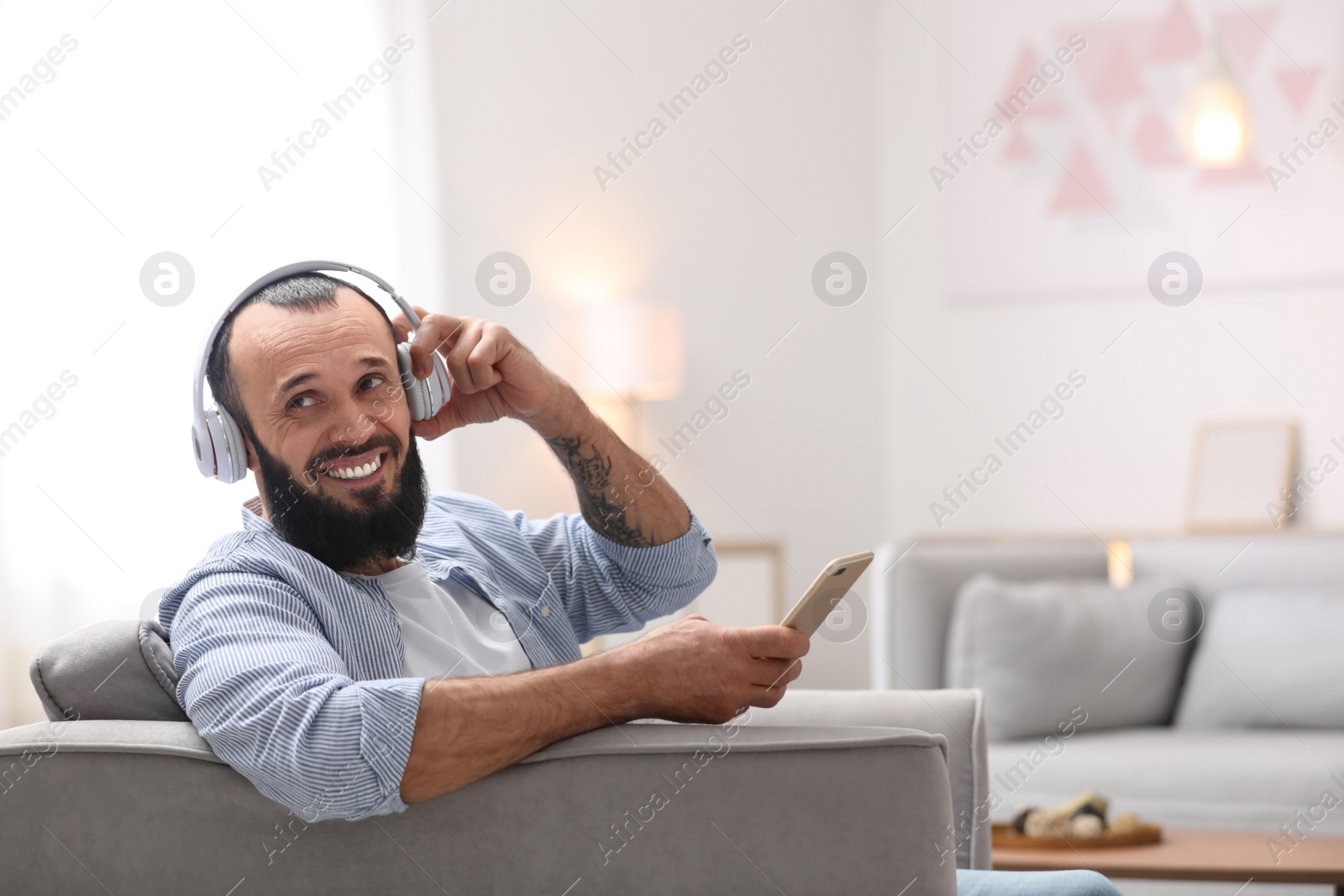 Photo of Mature man with headphones and mobile device resting in armchair at home