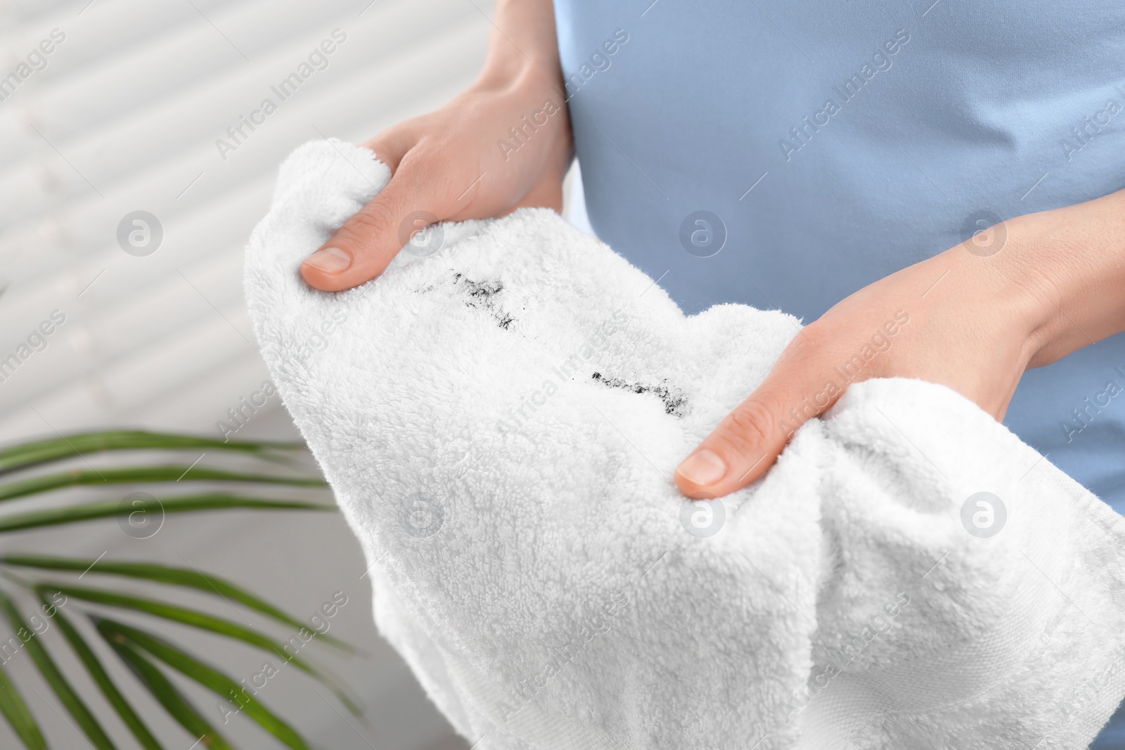 Photo of Woman holding terry towel with mascara spot indoors, closeup. Makeup removal