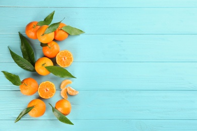 Fresh ripe tangerines with leaves on light blue wooden table, flat lay. Space for text