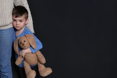 Photo of Sad little boy with toy hugging his mother on black background, space for text