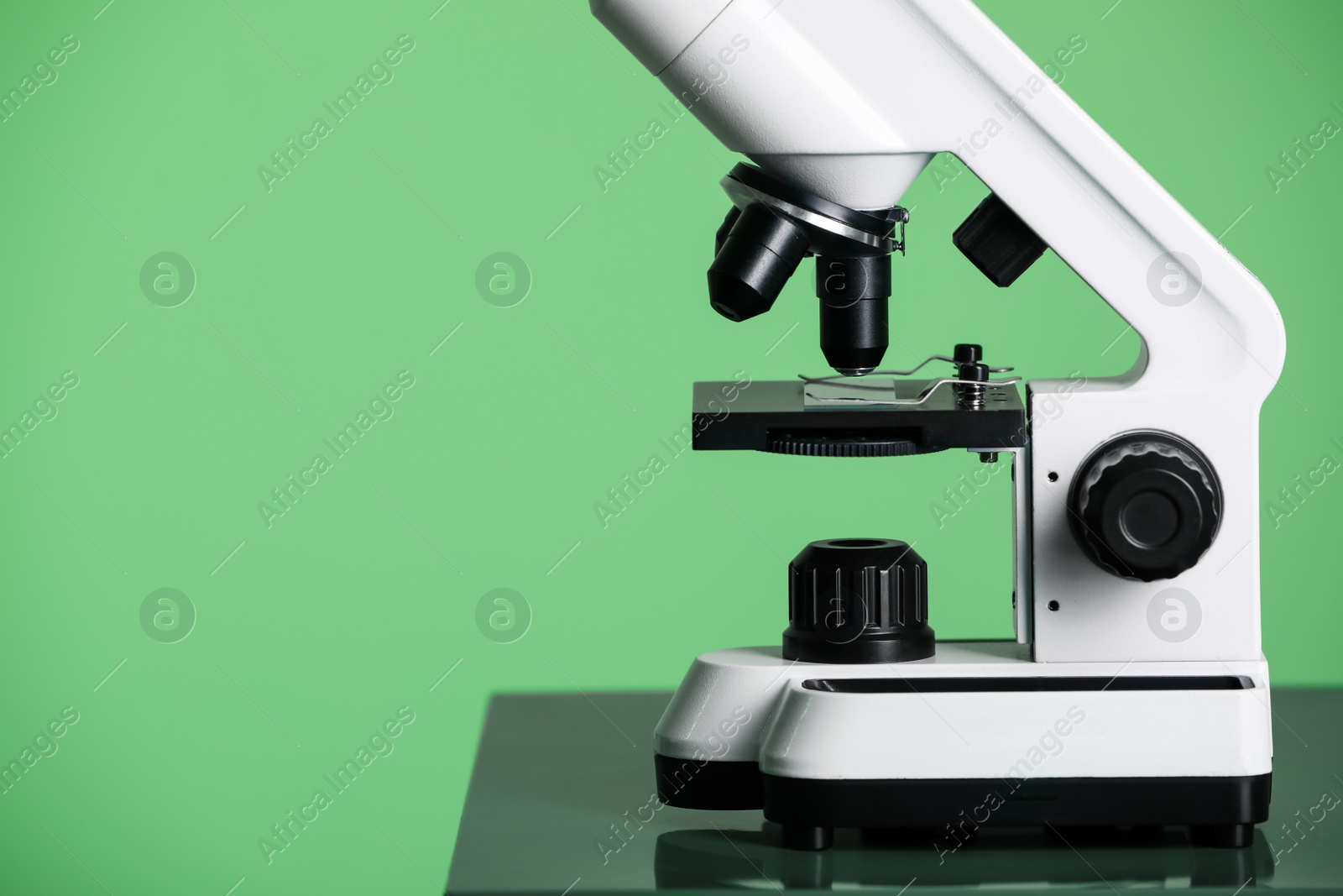 Photo of Modern medical microscope on table against green background, closeup. Space for text