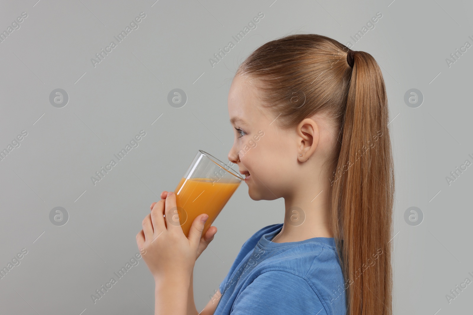 Photo of Cute little girl drinking fresh juice on light gray background, space for text