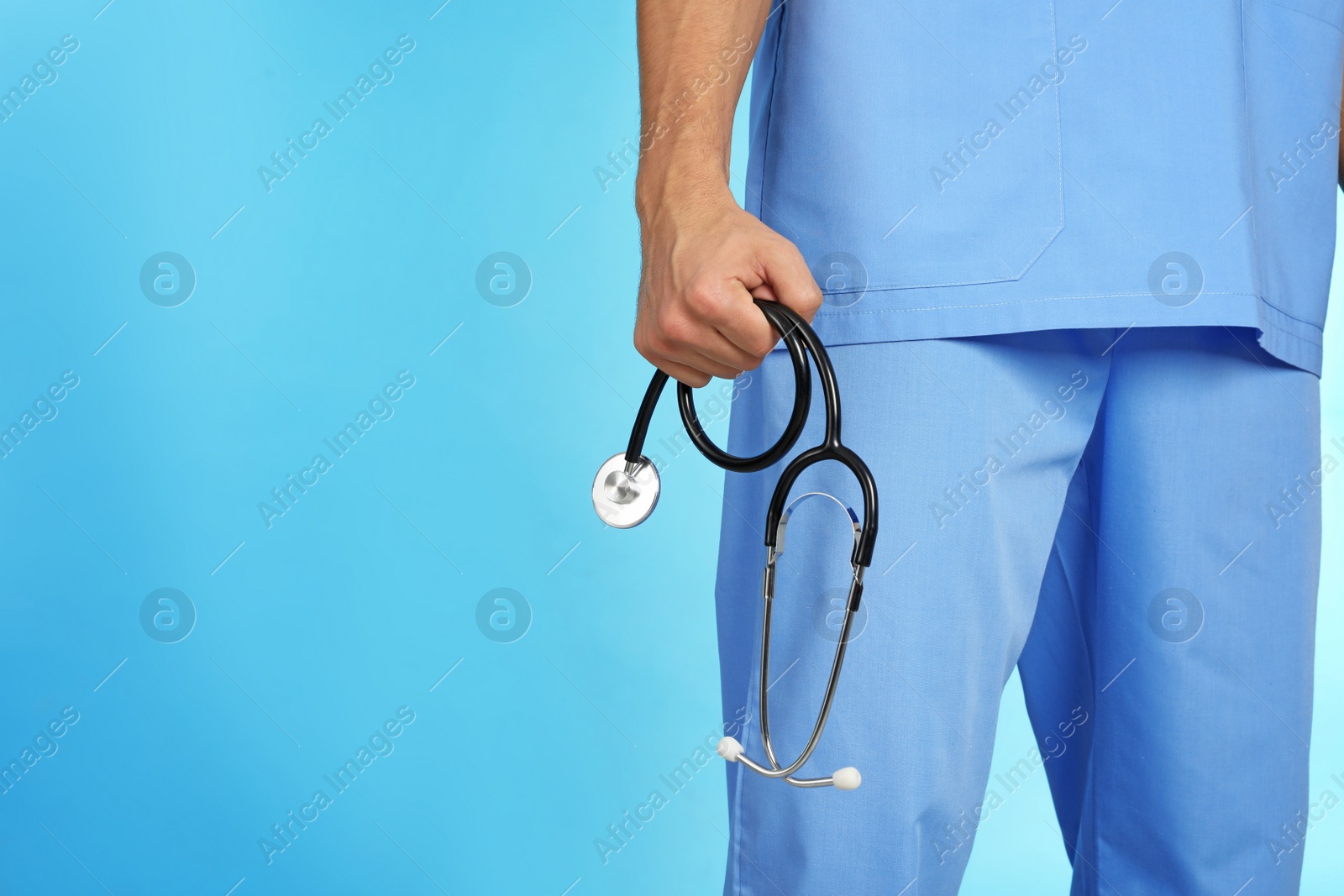 Photo of Male doctor holding stethoscope on color background, closeup with space for text. Medical object