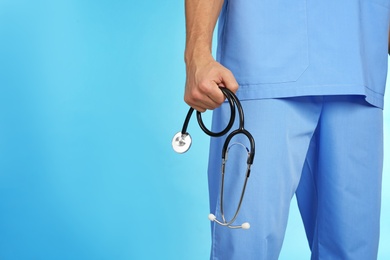 Photo of Male doctor holding stethoscope on color background, closeup with space for text. Medical object