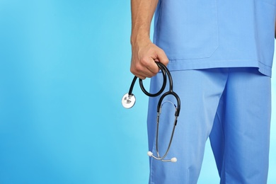 Male doctor holding stethoscope on color background, closeup with space for text. Medical object