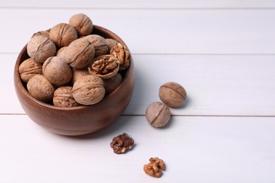 Photo of Bowl of walnuts on white wooden table. Space for text
