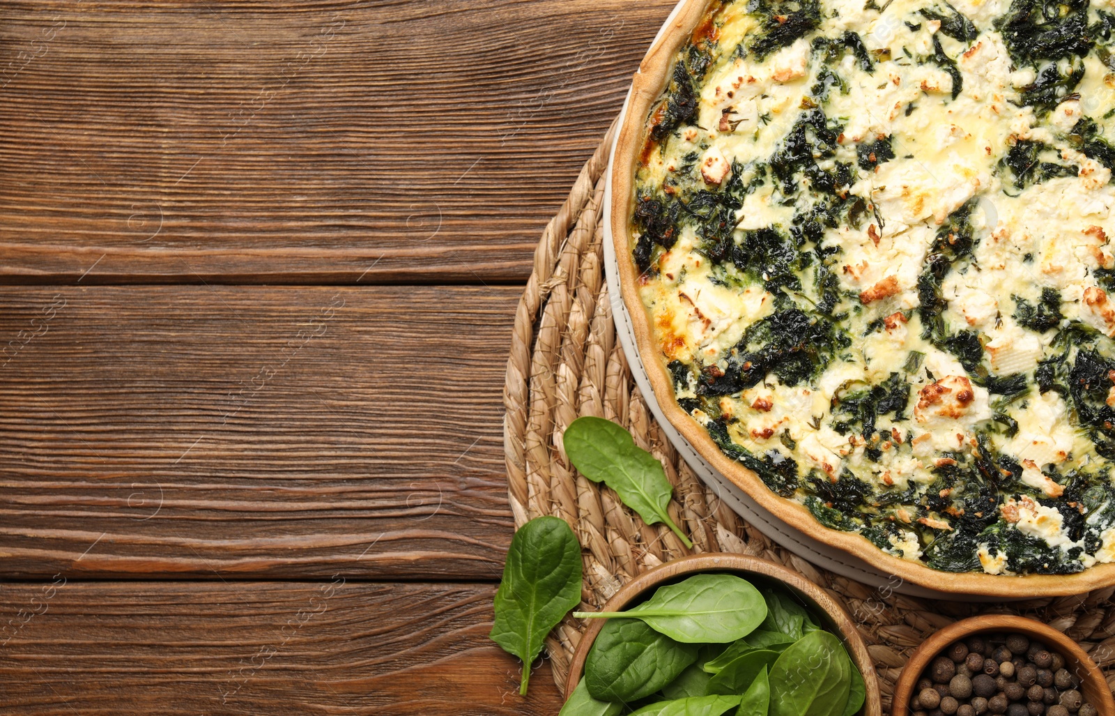 Photo of Delicious homemade quiche and spinach leaves on wooden table, flat lay. Space for text