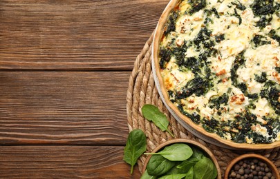 Delicious homemade quiche and spinach leaves on wooden table, flat lay. Space for text
