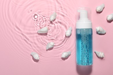 Bottle of facial cleanser and seashells in water against pink background, flat lay