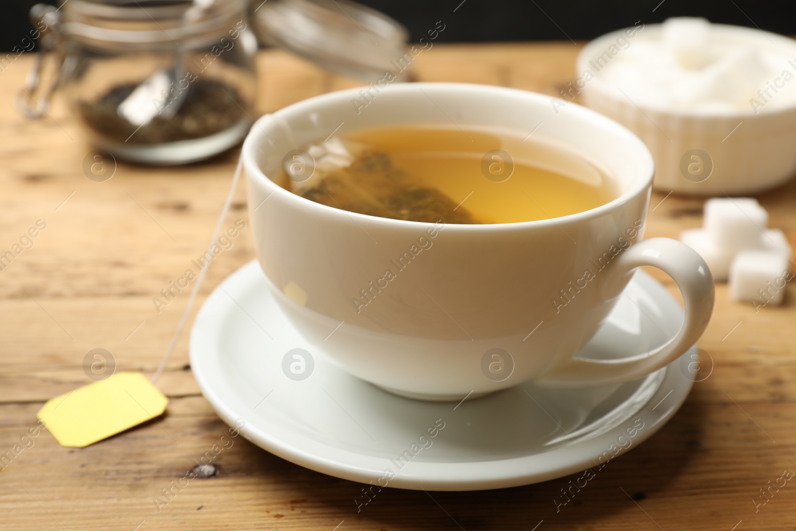 Photo of Tea brewing. White cup with tea bag on wooden table, closeup