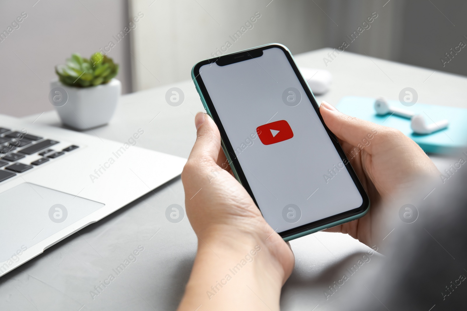 Photo of MYKOLAIV, UKRAINE - JULY 10, 2020: Woman holding Iphone 11 with Youtube app on screen at table, closeup