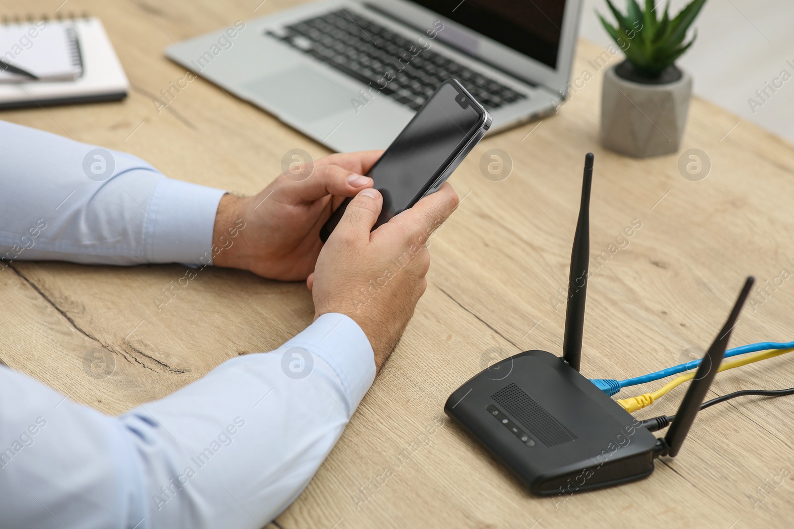 Photo of Man with smartphone and laptop connecting to internet via Wi-Fi router at wooden table, closeup