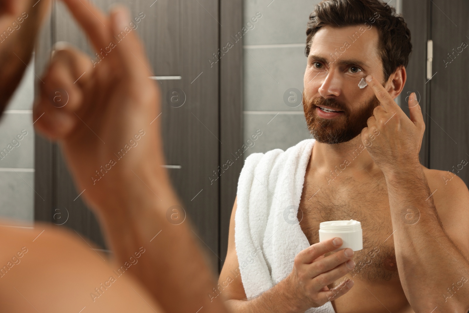 Photo of Handsome man applying cream on face in bathroom near mirror