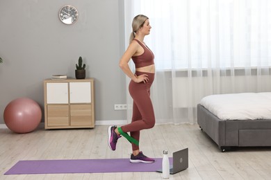 Online fitness trainer. Woman doing exercise with elastic band near laptop at home