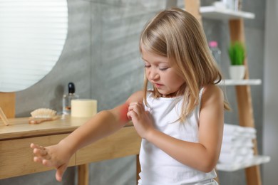 Photo of Suffering from allergy. Little girl scratching her arm in bathroom