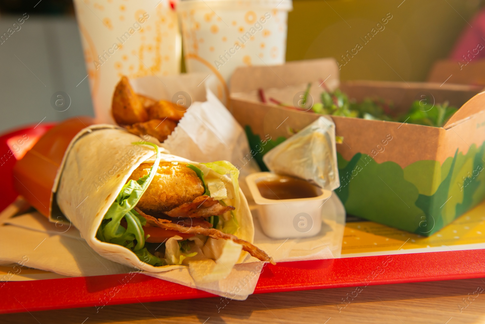 Photo of WARSAW, POLAND - SEPTEMBER 16, 2022: Roll with chicken, fried potatoes and salad on table in McDonald's cafe, closeup