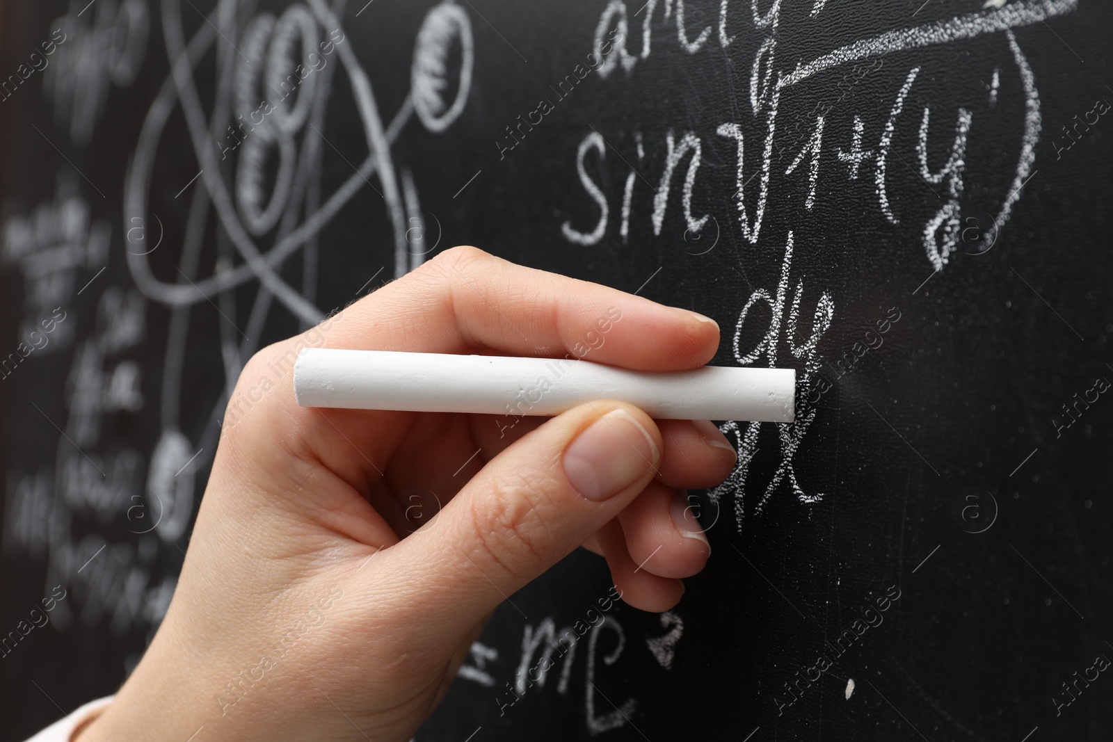 Photo of Teacher writing math formulas with chalk on blackboard, closeup