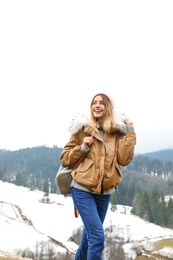 Young woman in warm clothes near snowy hill. Winter vacation